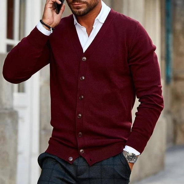 Man in bordeauxrode cardigan met knopen, witte overhemdkraag zichtbaar, pratend op smartphone. Stijlvolle herenkleding, casual mode.