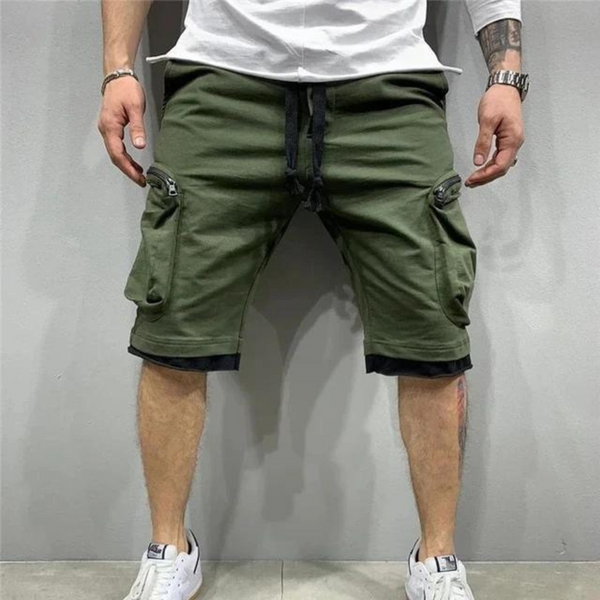 Man draagt groene cargo shorts met zakken en ritsen, gecombineerd met witte sneakers en een wit shirt. Trendy herenkleding, casual stijl.