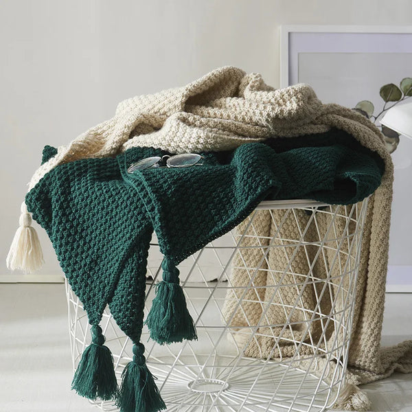 Groene en beige gebreide dekens met kwastjes in een witte draadmand, decoratief interieuraccessoire, moderne woondecoratie, gezellige textielstijl.