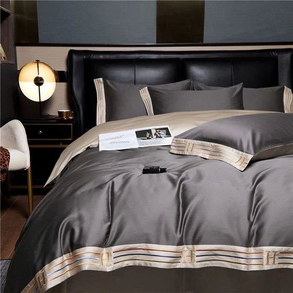 Luxe grijs dekbedovertrek op kingsize bed met gouden accenten, moderne slaapkamerinrichting, nachtkastje met lamp, comfortabele stoel.