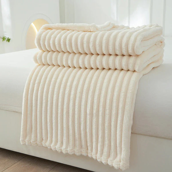 Zachte, crèmekleurige fleece deken op bed, gestapeld en geribbeld. Perfect voor slaapkamerdecoratie en extra warmte. Luxe en comfort in huis.