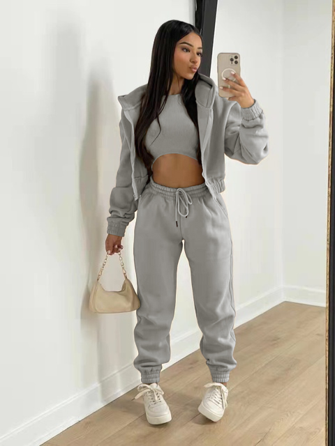 Vrouw in grijs trainingspak met crop top en hoodie, poseert voor spiegel met smartphone. Casual mode, comfortabele loungewear, trendy outfit.