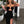 Vrouw in elegante zwarte avondjurk met hoge split en cut-out detail, houdt een cocktailglas vast. Perfect voor feestelijke gelegenheden en mode-inspiratie.