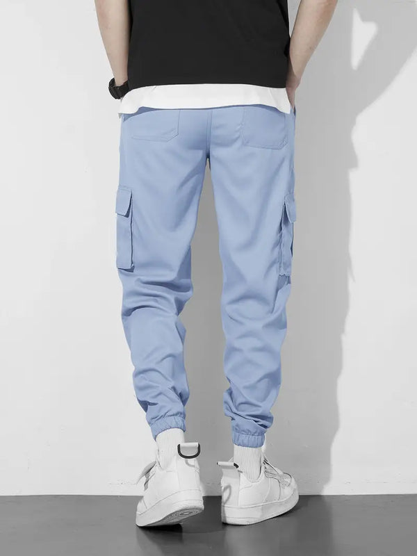 Man in lichtblauwe cargobroek met zakken, witte sneakers en zwart-wit T-shirt. Casual herenkleding, modetrend, comfortabele stijl.