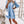 Vrouw in lichtblauwe denim jurk met halflange mouwen, A-lijn patroon, boven de knie, gecombineerd met witte sneakers en tas, modieuze casual look.