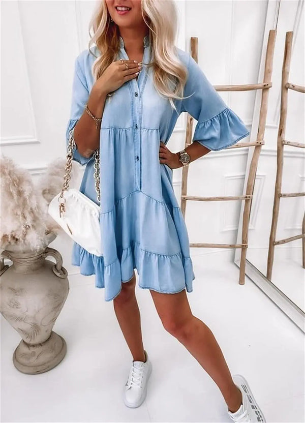 Vrouw in lichtblauwe denim jurk met halflange mouwen, A-lijn patroon, boven de knie, gecombineerd met witte sneakers en tas, modieuze casual look.