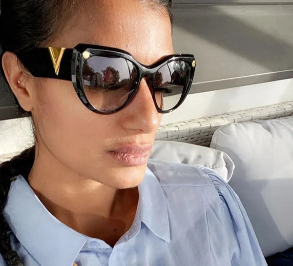 Vrouw draagt luxe oversized zwarte zonnebril met gouden details, modieus ontwerp, ideaal voor damesmode en zomeraccessoires.