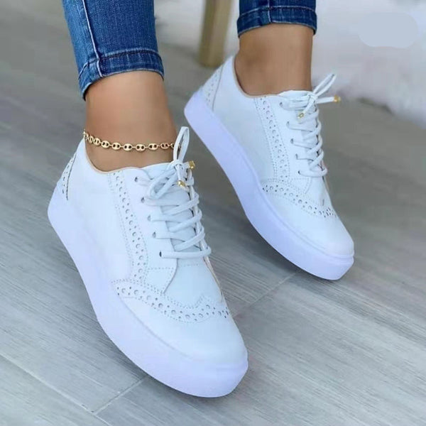 Witte dames sneakers met veters, lage top en ronde neus, gedragen met blauwe jeans. Casual gevulkaniseerde schoenen voor dagelijks gebruik.