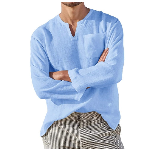 Man in lichtblauw linnen overhemd met borstzak, gekruiste armen, gestreepte broek. Casual zomeroutfit, herenmode, comfortabele kledingstijl.