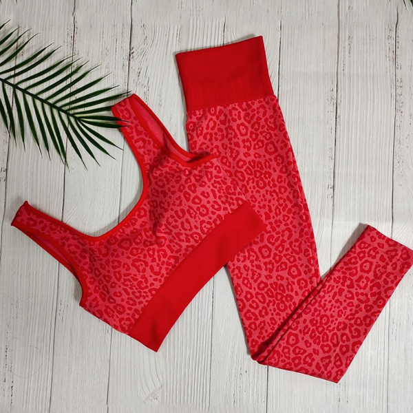 Rode luipaardprint sportbeha en legging set op witte houten vloer met palmblad. Perfect voor yoga, fitness en actieve damesmode.