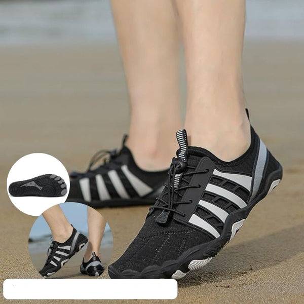 Zwarte waterschoenen met grijze strepen op zandstrand, ideaal voor outdooractiviteiten. Lichtgewicht, ademend en slipvast ontwerp voor comfort en veiligheid.