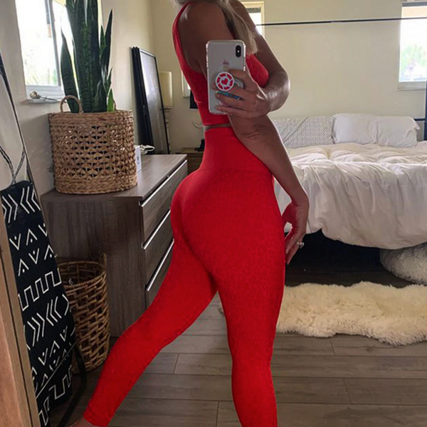 Vrouw in rode sportlegging en top poseert voor spiegel in slaapkamer. Fitnesskleding, sportoutfit, actieve levensstijl, thuisworkout.