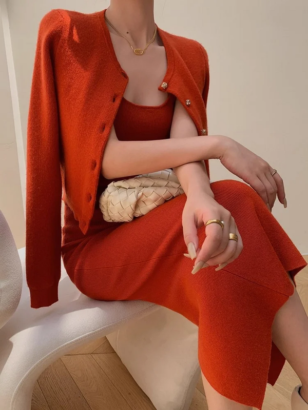 Vrouw in stijlvolle rode jurk en vest, zittend op moderne stoel, met witte gevlochten tas. Elegante mode, minimalistisch design, trendy outfit.