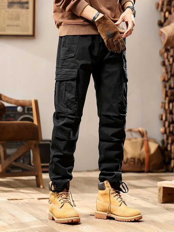 Man in casual outfit met zwarte cargobroek en bruine werklaarzen, staand in een moderne woonkamer. Stijlvolle herenkleding, comfortabele vrijetijdskleding.