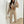 Vrouw in beige joggingpak met crop top, witte sneakers en kleine handtas, poseert voor spiegel. Modieuze casual outfit, trendy dameskleding.