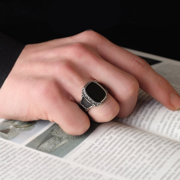 Hand met zilveren zegelring met zwarte steen, rustend op een open boek. Stijlvolle herenring, vintage design, sieradenaccessoire, elegantie.
