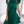 Vrouw in groene geplooide jurk met strik en pofmouwen, draagt witte schoudertas met gouden ketting. Stijlvolle mode, elegante dameskleding.