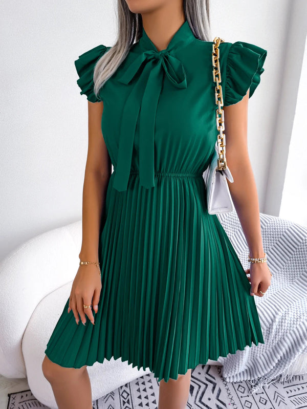 Vrouw in groene geplooide jurk met strik en pofmouwen, draagt witte schoudertas met gouden ketting. Stijlvolle mode, elegante dameskleding.