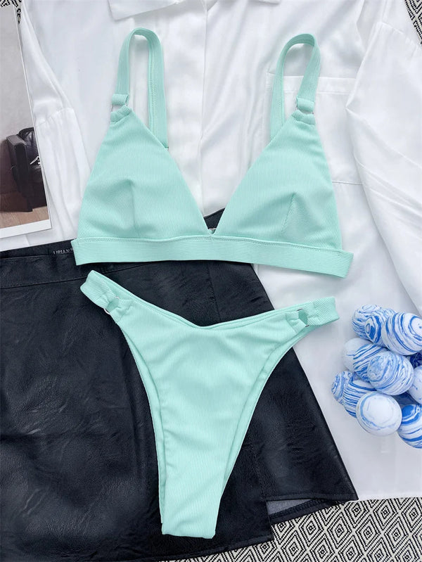 Mintgroene bikini set met triangel top en hoge taille slip, liggend op een witte blouse en zwarte rok. Perfect voor strandmode en zomerse stijl.