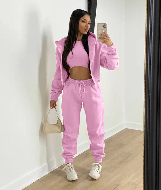 Vrouw in roze trainingspak met crop top, houdt een beige handtas vast en maakt een selfie in een moderne kamer. Sportieve mode, casual outfit.