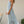 Vrouw in lichtblauwe maxi-jurk, staand naast houten stoel in tuin. Zomerse mode, elegante kleding, casual stijl, buitenomgeving.