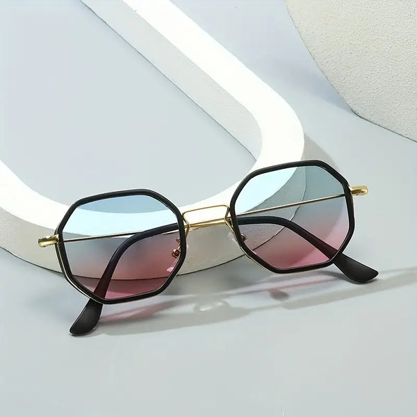 Zwarte zeshoekige zonnebril met goudkleurige accenten en roze-blauwe glazen op een grijze achtergrond. Trendy unisex zonnebril voor zomer 2023.