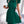 Vrouw in groene geplooide jurk met strik, gouden kettingtas, witte achtergrond. Elegante damesmode, zomerjurk, trendy kledingstijl.