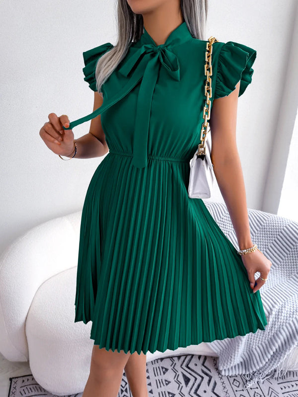 Vrouw in groene geplooide jurk met strik, gouden kettingtas, witte achtergrond. Elegante damesmode, zomerjurk, trendy kledingstijl.