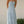 Vrouw in lichtblauwe zomerjurk met halternek, staand in tuin. Elegante maxi-jurk, perfect voor zomerse gelegenheden. Modetrends 2023.