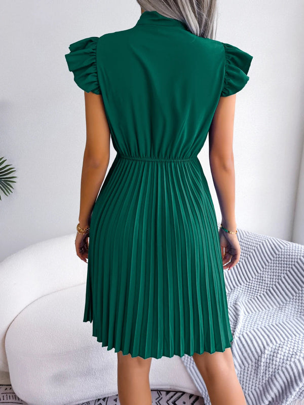 Groene geplooide jurk met korte mouwen, gedragen door een vrouw, gefotografeerd van achteren. Perfect voor zomermode en elegante casual looks.
