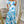 Vrouw in blauwe en witte bloemenjurk met cut-out details, staand voor een spiegel in een elegante kamer. Zomerjurk, modetrend, dameskleding.