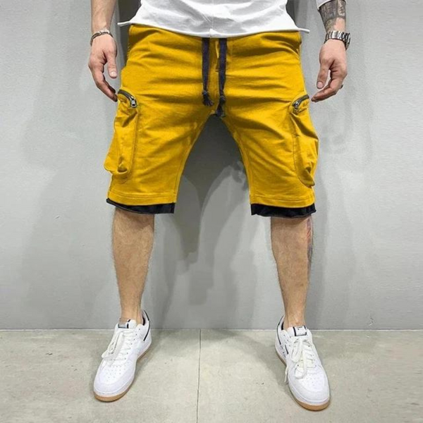 Man in gele cargoshorts en witte sneakers tegen grijze achtergrond. Modieuze zomerkleding, casual stijl, comfortabele herenshorts.