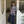 Vrouw in grijze cardigan en lange zwarte rok poseert in deuropening van stijlvolle boetiek. Mode, casual outfit, trendy kledingstijl.