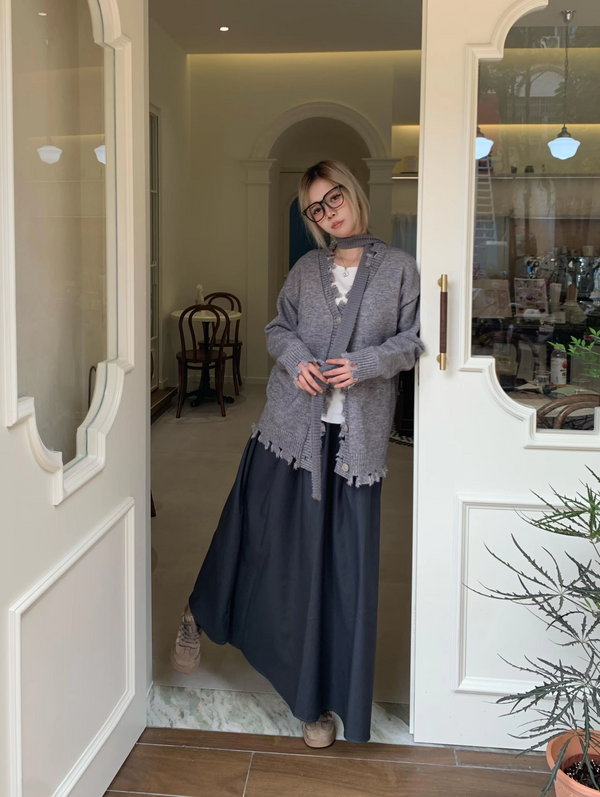 Vrouw in grijze cardigan en lange zwarte rok poseert in deuropening van stijlvolle boetiek. Mode, casual outfit, trendy kledingstijl.
