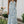 Vrouw in blauwe bloemenjurk met halternek, staand in tuin naast houten tafel met rozen. Zomermode, elegante dameskleding, casual stijl.