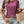Vrouw in paarse top met korte mouwen, denim shorts en gevlochten rieten tas. Accessoires: armbanden en kettingen. Casual zomeroutfit.