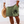 Man in witte blouse en groene korte broek met berenpootafdruk, strandachtergrond, zomermode, strandkleding, casual herenkleding.