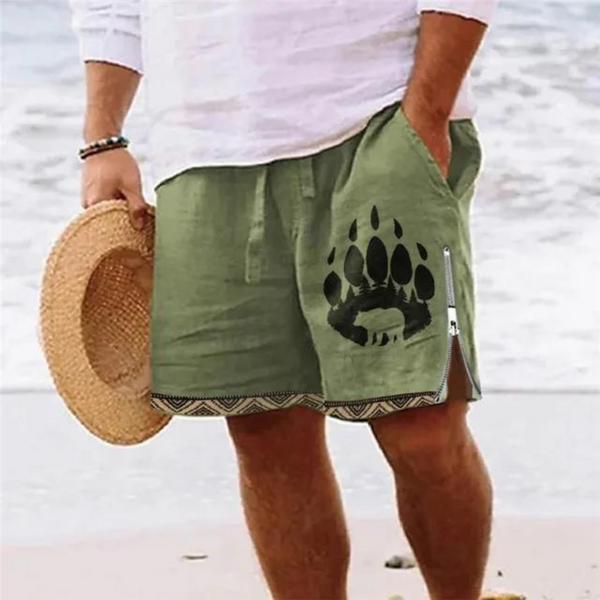 Man in witte blouse en groene korte broek met berenpootafdruk, strandachtergrond, zomermode, strandkleding, casual herenkleding.