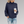 Vrouw in donkerblauwe gebreide trui met koffiebeker, casual outfit, gescheurde jeans, grijze achtergrond. Perfect voor herfstmode en comfort.