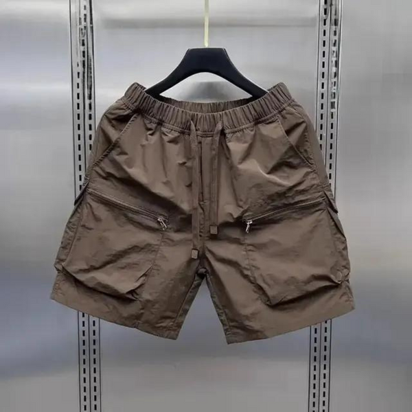Bruine cargoshorts met meerdere zakken, ritssluitingen en elastische tailleband, hangend aan een zwarte hanger in een metalen kast.