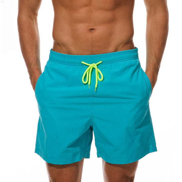 Turquoise zwembroek met felgele veter, gedragen door een man. Perfect voor strandmode en zomerse activiteiten. Comfortabel en stijlvol ontwerp.