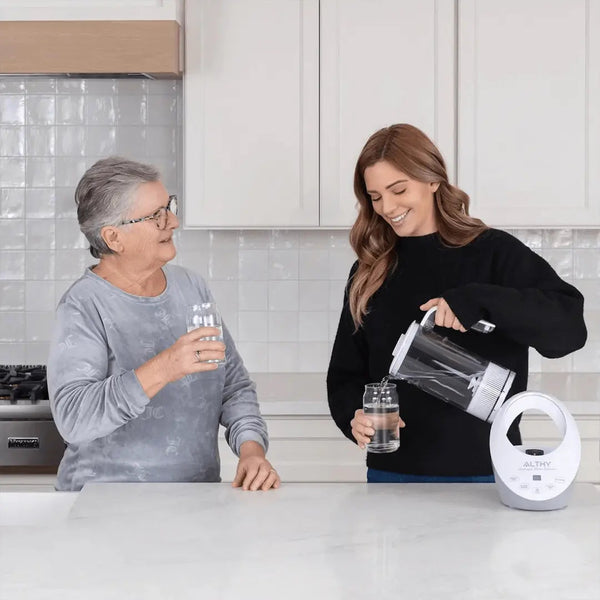 Twee vrouwen in moderne keuken met Althy waterfilterkan, water inschenken in glazen. Gezond drinkwater, keukenapparatuur, waterzuivering.