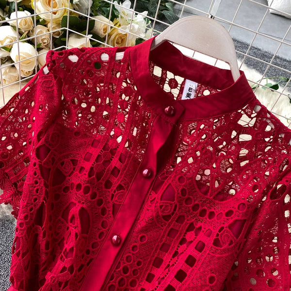 Rode kanten blouse met knoopsluiting, gedetailleerd patroon, op een hanger voor een achtergrond van witte rozen. Perfect voor elegante mode.