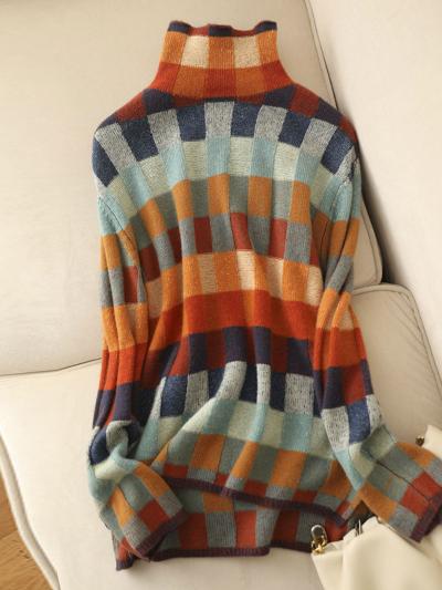 Gebreide coltrui met kleurrijk geruit patroon in blauw, oranje en beige tinten, liggend op een crèmekleurige bank. Modieuze herfstkleding.