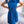 Vrouw in elegante blauwe plisséjurk met strik, staand voor witte bank. Mode, dameskleding, zomerjurk, stijlvolle outfit, trendy design.