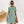 Vrouw in groen-wit gestreepte jurk met zonnebril en rieten tas, tegen witte achtergrond. Zomermode, casual dameskleding, trendy outfit.