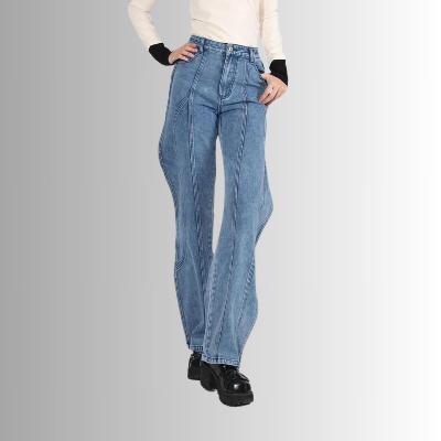 Vrouw draagt blauwe wijde jeans met hoge taille en zwarte laarzen, tegen een grijze achtergrond. Modieuze dameskleding, casual stijl.