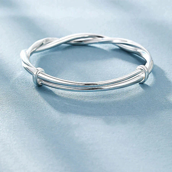Zilveren armband met gedraaide details op een lichtblauwe achtergrond, elegant en modern ontwerp, perfect voor dames sieraden collectie.