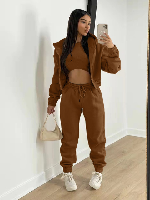 Vrouw in bruine joggingpak met crop top, houdt beige handtas vast, maakt selfie in moderne kamer. Trendy damesmode, comfortabele loungewear.