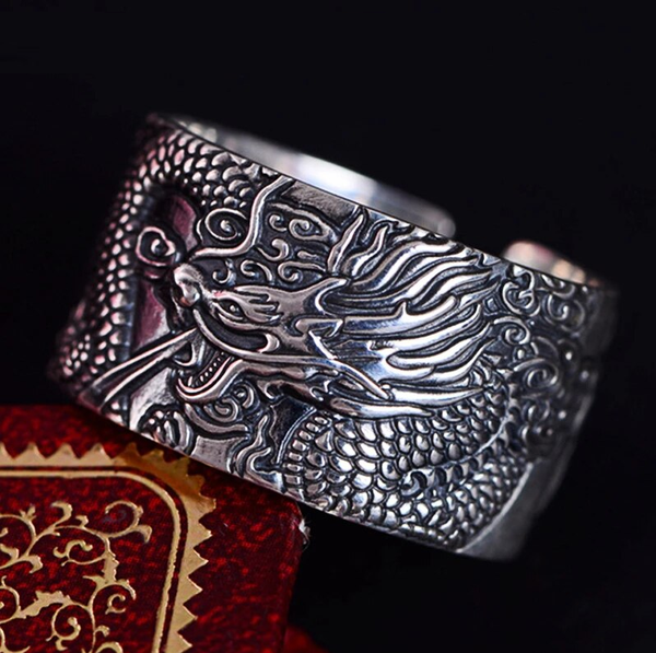 Zilveren ring met drakenmotief, gedetailleerd gegraveerd, op een rode achtergrond. Perfect voor liefhebbers van draken sieraden en unieke accessoires.